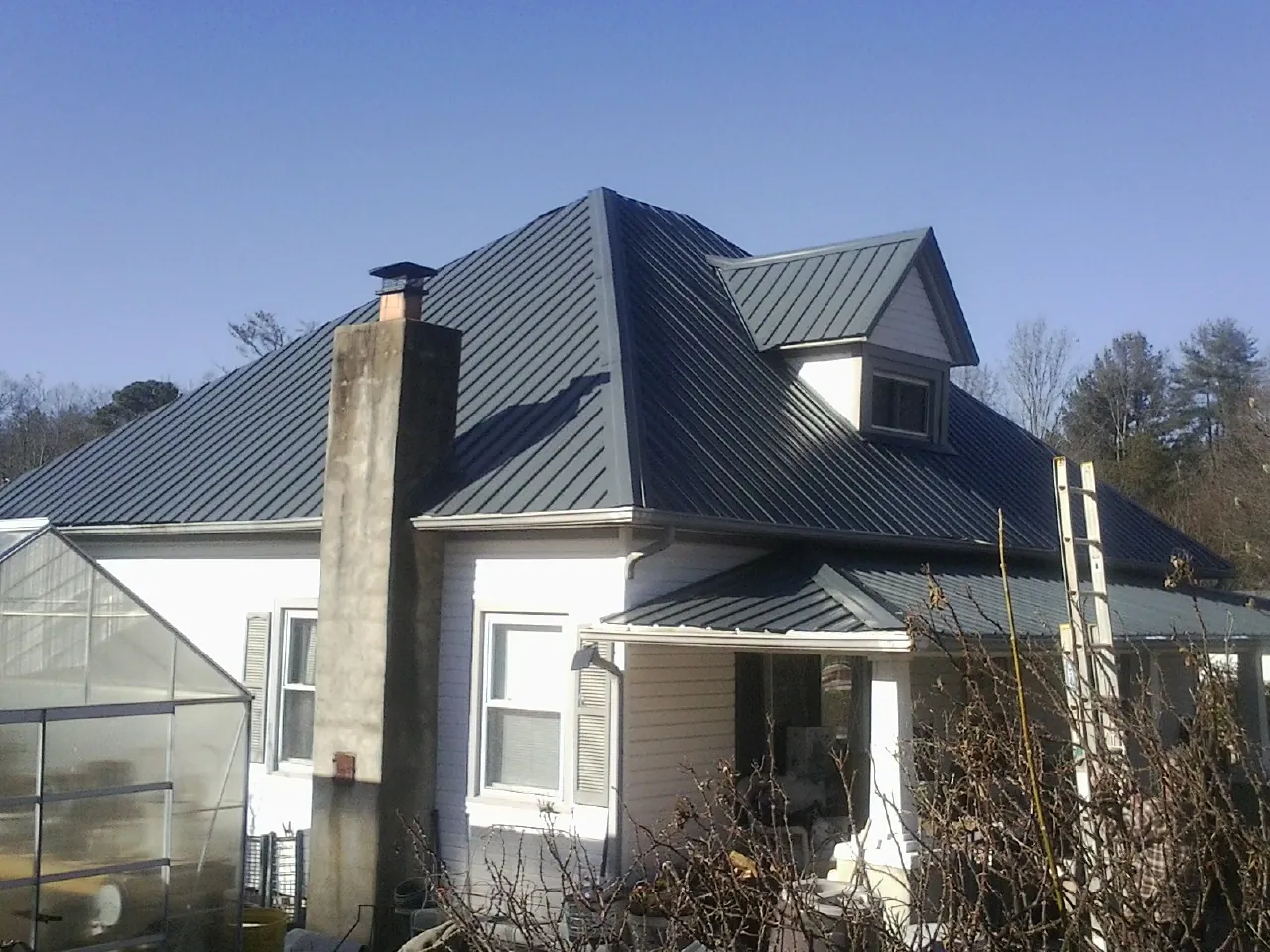 Dark blue standing seam metal roof on a white farmhouse with dormer — Slate & Tile Roof Repair by Roofing Brothers in Cottageville