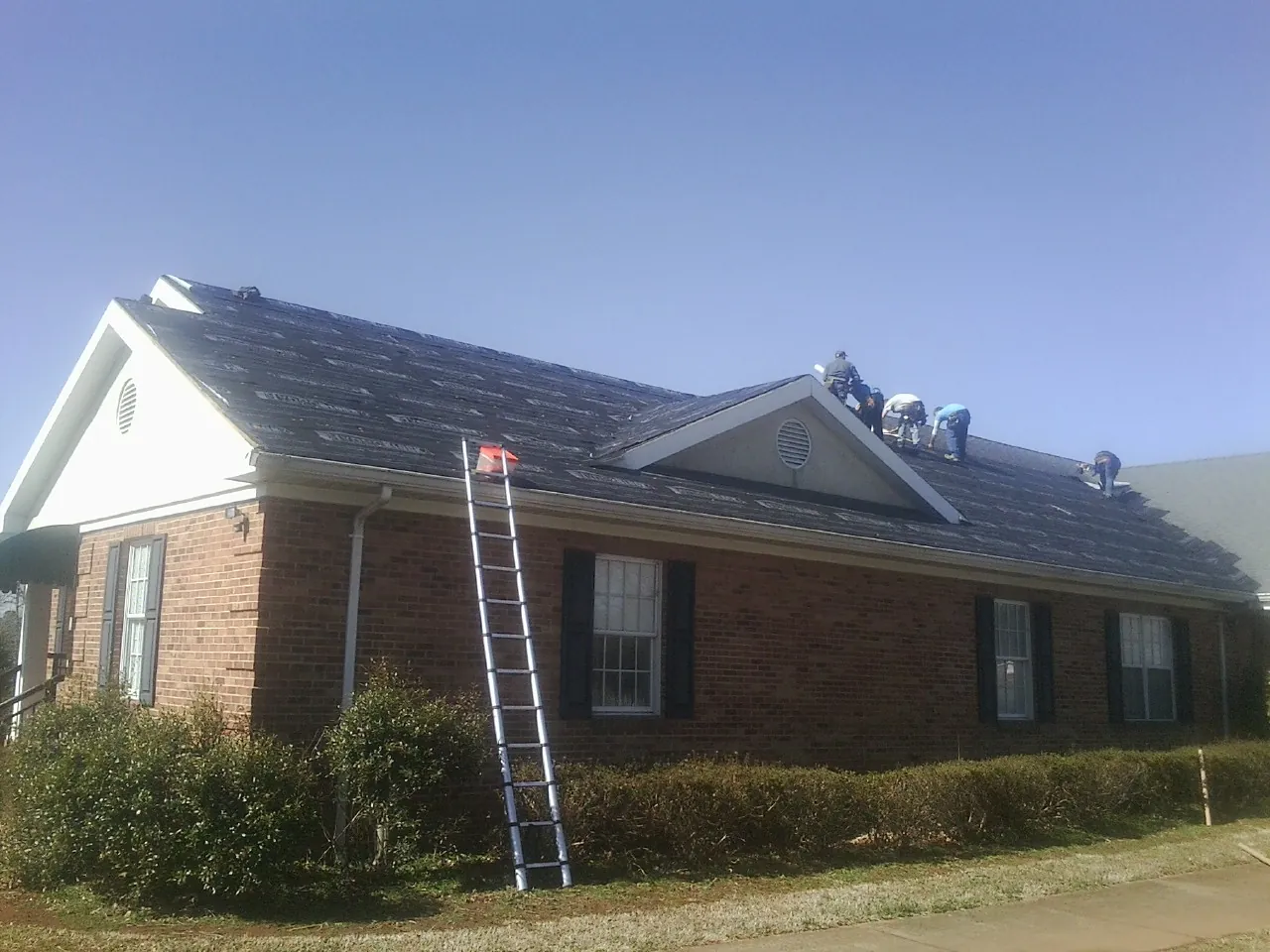 Crew tearing shingles off a brick ranch roof with a ladder set — Emergency Roof Repair work by our crew in Cottageville