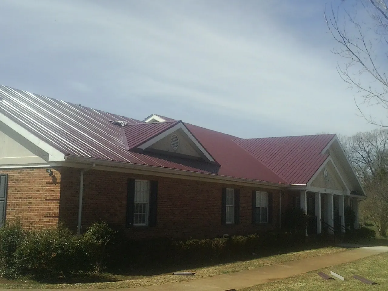 Red metal roof with gabled entries on a long brick building, from a Hail Damage Roof Repair job in Cottageville