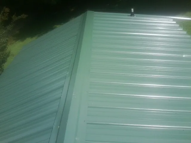 New green metal panels meeting at the ridge of a roof — Flat Roof Repair work by our crew in Cottageville