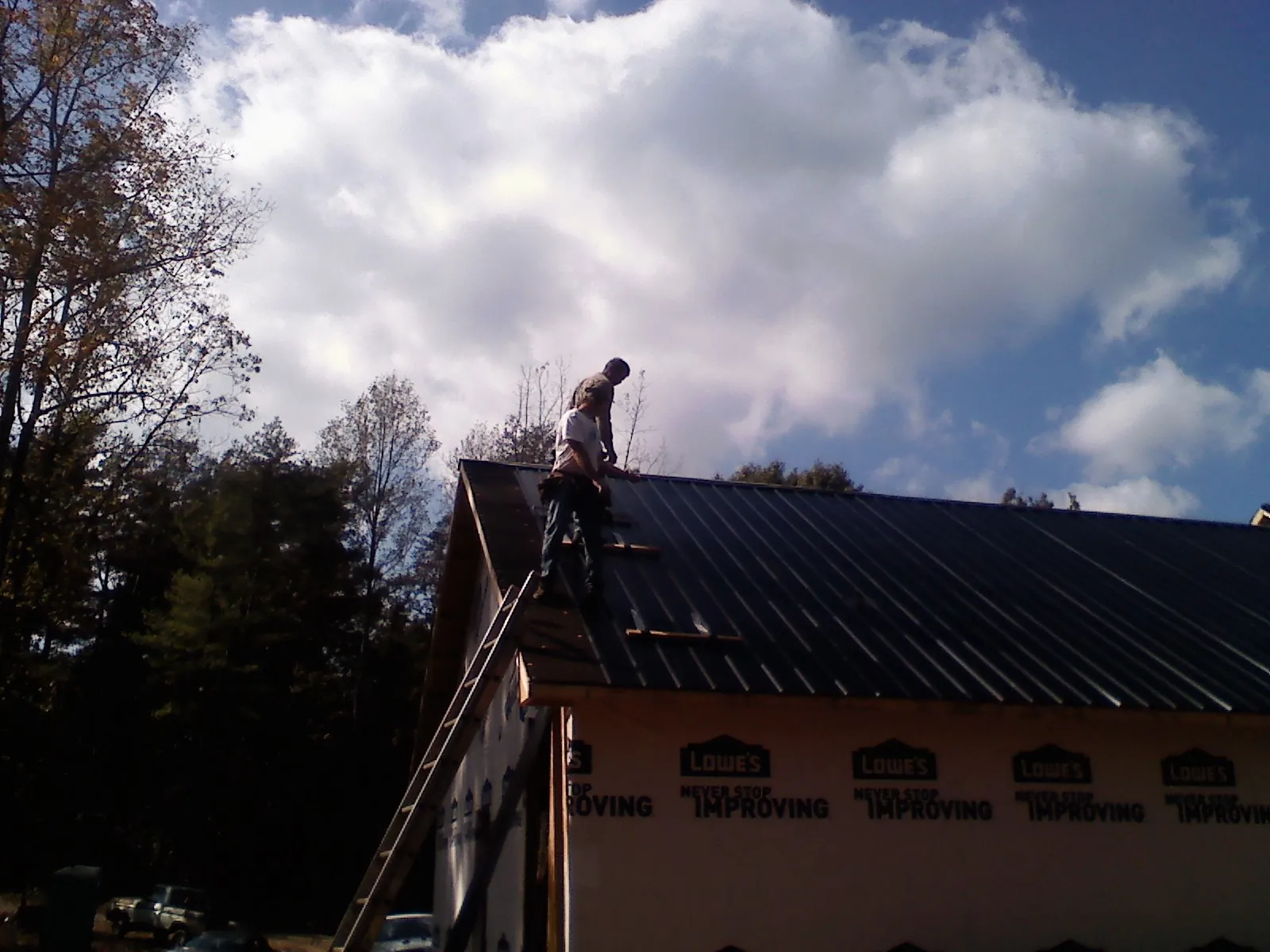 Roofer fastening dark metal panels high against a cloudy sky, from a Roof Inspection job in Cottageville