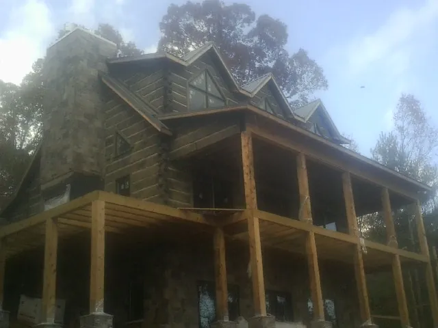 Stone chimney and dormers on a large log home with a timber porch in Cottageville