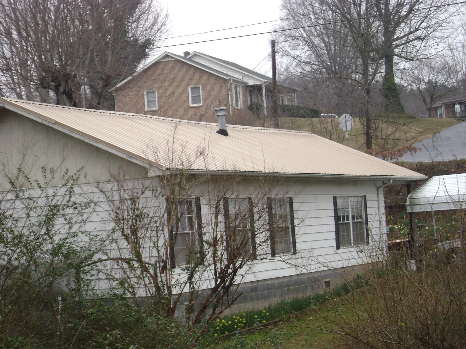 Tan metal roof on a white sided house set into a hillside — Commercial Roofing by Roofing Brothers in Cottageville